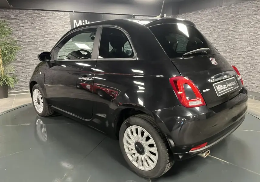 Fiat 500 noire vue en 3/4 arrière droit, avec jantes alliage et feux arrière distinctifs dans un showroom.