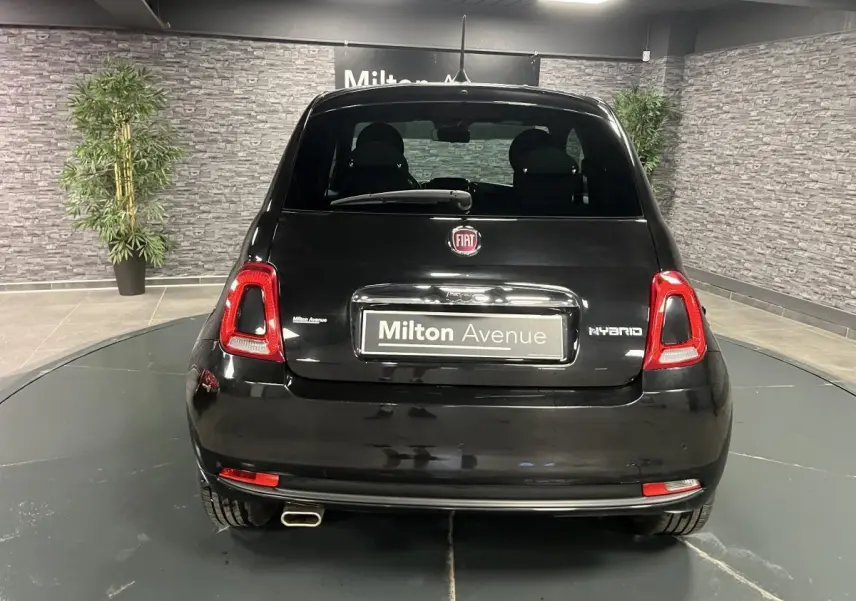 Vue arrière d'une Fiat 500 noire hybride 2023 avec logo FIAT et plaque Milton Avenue dans un showroom.