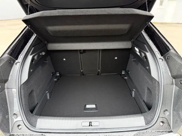 Coffre ouvert vu de l'arrière d'un Peugeot 3008 Hybrid 145 GT gris titane, montrant un espace de chargement spacieux et propre.