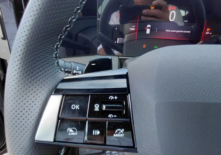 Gros plan sur le volant perforé et les commandes multifonctions de l’Opel Astra noire, avec tableau de bord numérique en arrière-plan.