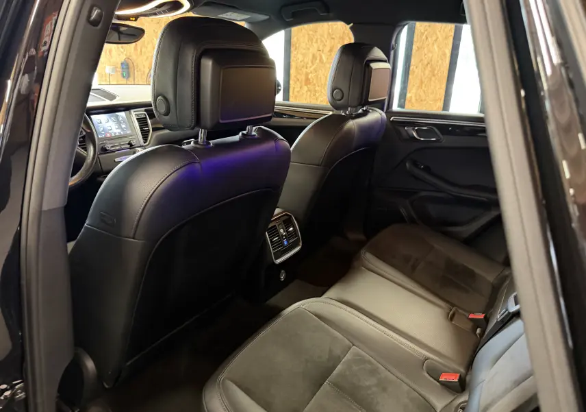 Vue intérieure arrière droite du Porsche Macan S noir, sièges cuir et alcantara, ventilation arrière et tableau de bord tactile visible.