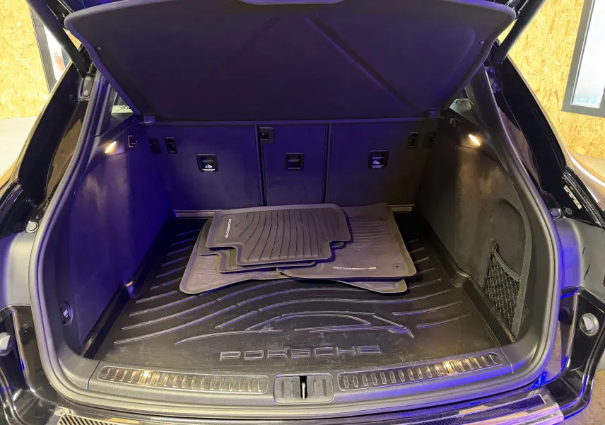 Coffre ouvert vu de l'arrière d'un Porsche Macan S noir avec tapis de sol Porsche et éclairage intérieur.