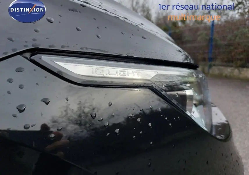 Gros plan sur le phare avant droit noir métal de la Volkswagen Golf 1.5 TSI 150ch 2024 avec pluie visible sur la carrosserie.