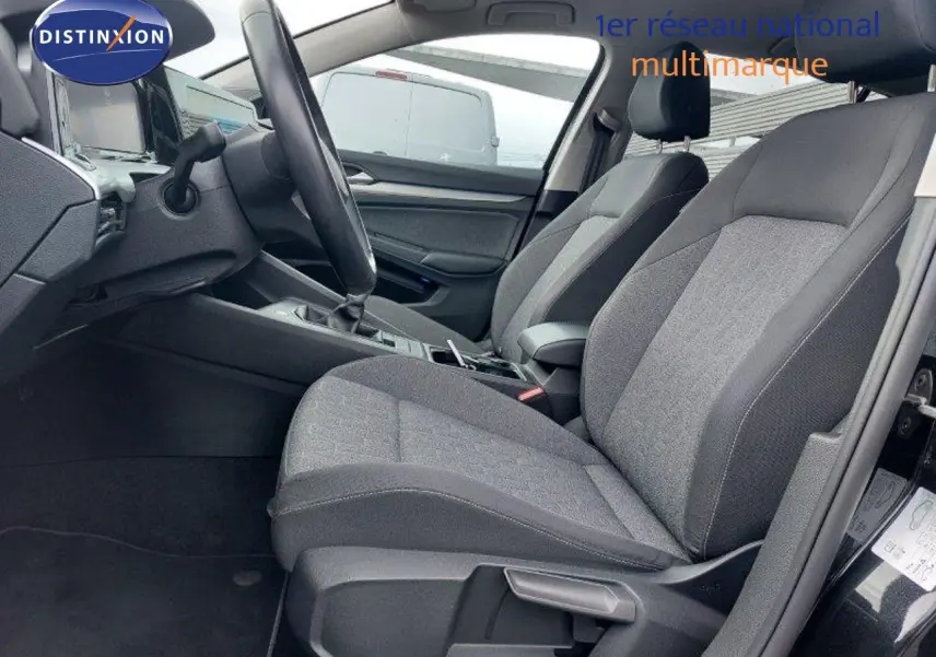 Vue intérieure côté conducteur d'une Volkswagen Golf 1.5 TSI noire, montrant les sièges tissu gris et la console centrale.