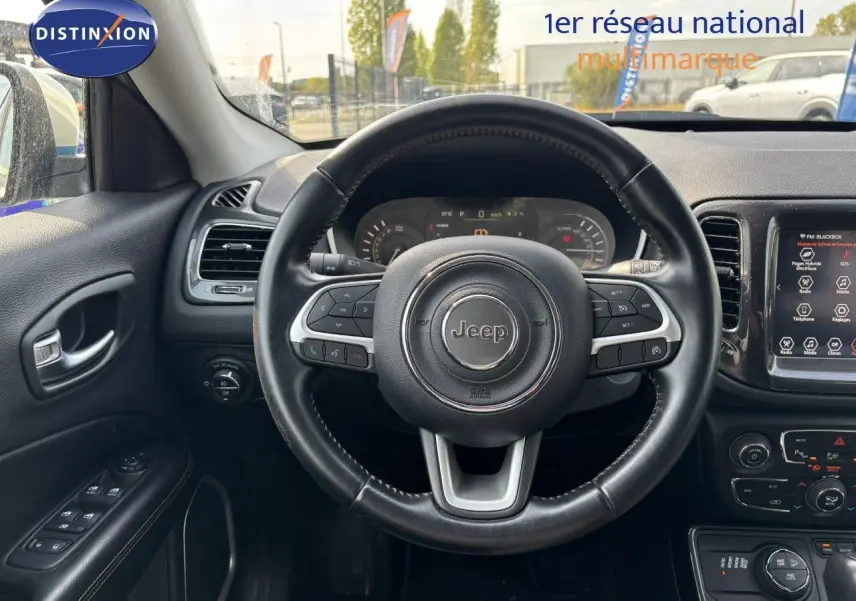 Vue intérieure centrée sur le volant cuir noir du Jeep Compass blanc, avec tableau de bord et écran tactile visibles.