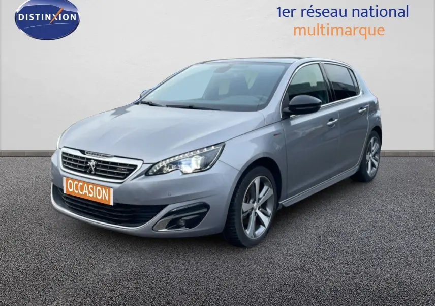 Peugeot 308 gris Artense vue 3/4 avant droit, avec phares allumés et jantes alliage distinctives.