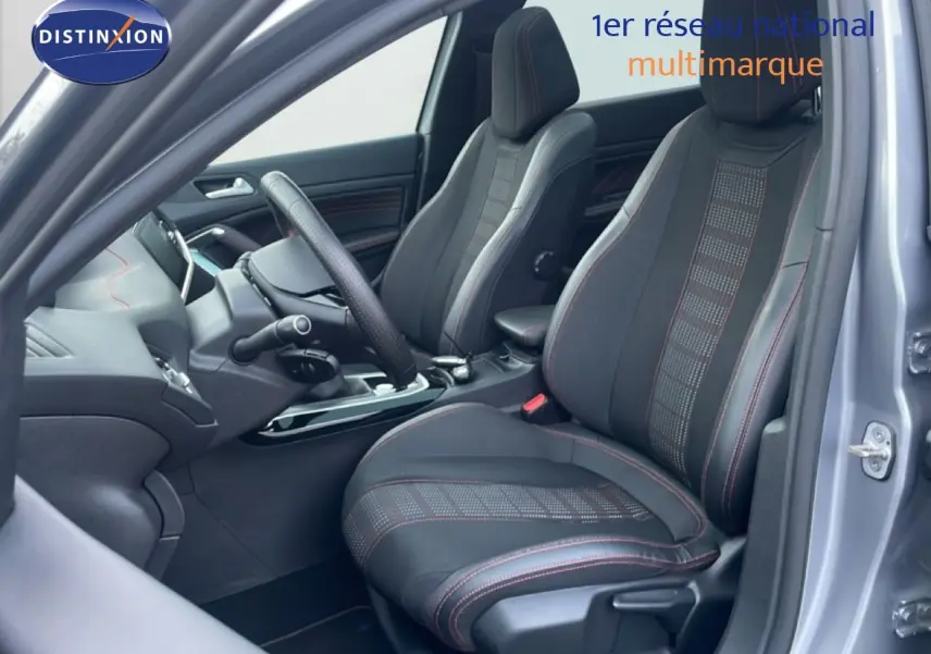 Vue intérieure côté conducteur de la Peugeot 308 gris Artense, sièges sport noirs avec surpiqûres rouges visibles.
