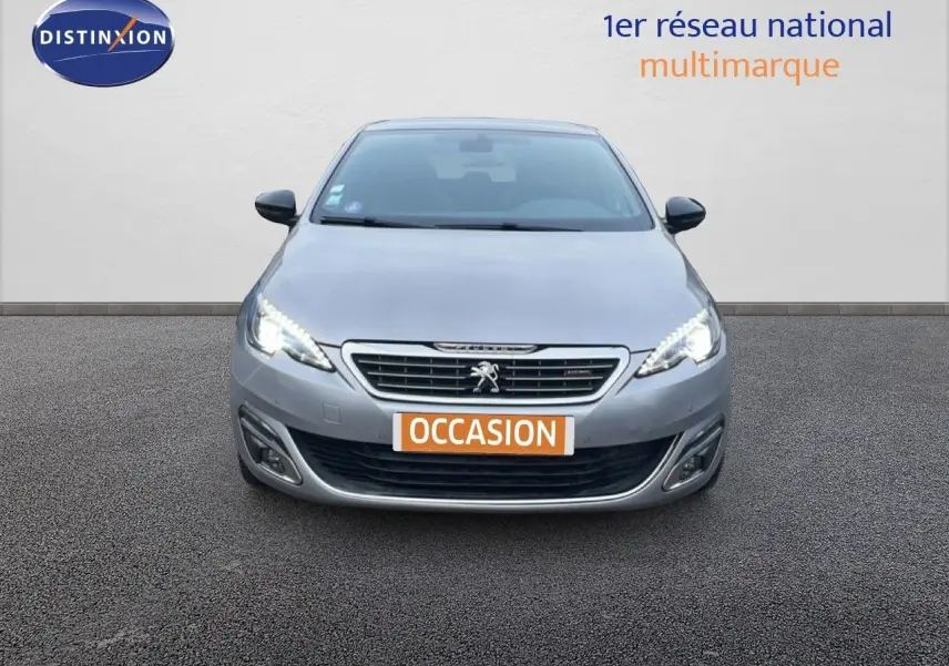 Vue de face d'une Peugeot 308 gris Artense avec phares LED allumés et plaque "OCCASION" visible.