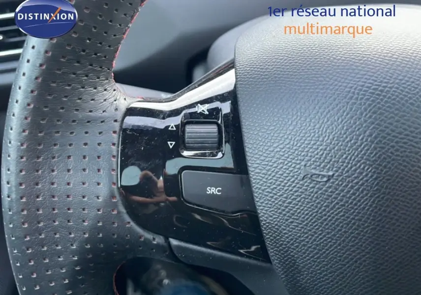 Gros plan sur la partie gauche du volant perforé noir de la Peugeot 308 gris Artense avec commandes audio intégrées.