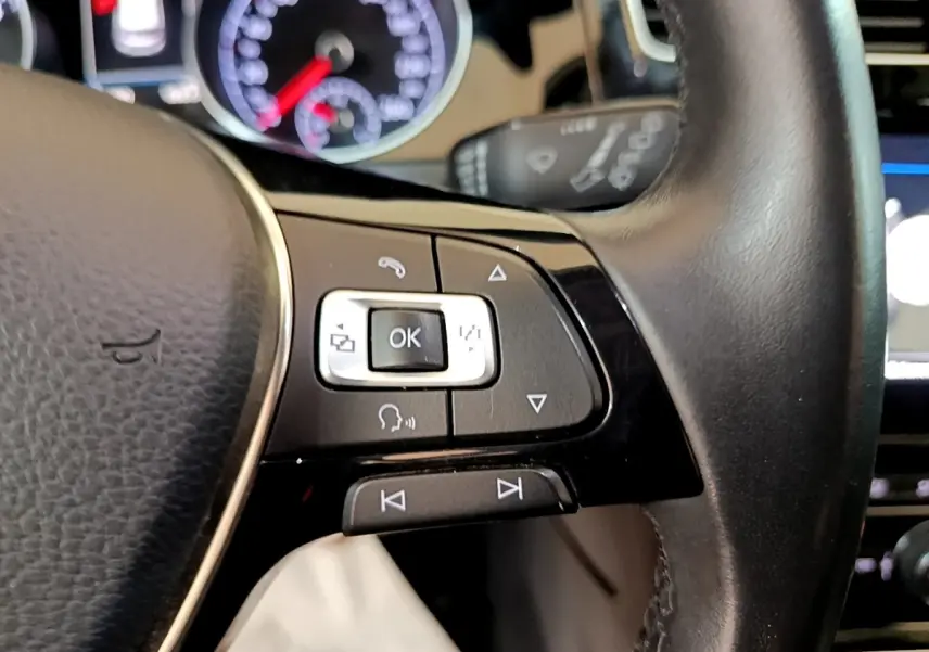 Gros plan sur les commandes gauche du volant cuir noir de la Volkswagen Golf gris clair, avec tableau de bord flou en arrière-plan.