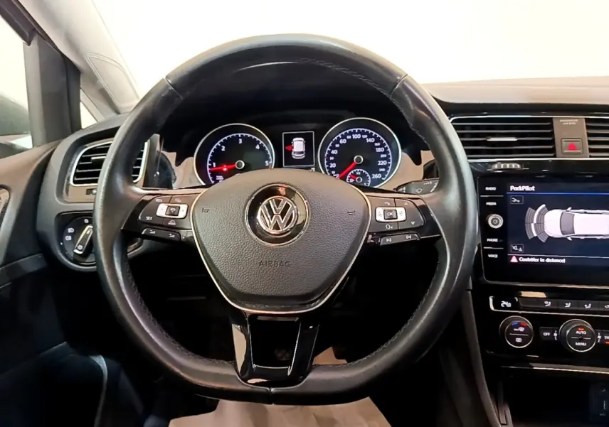 Vue frontale du volant cuir noir de la Volkswagen Golf 2017 avec tableau de bord et écran tactile affichant l'aide au stationnement.