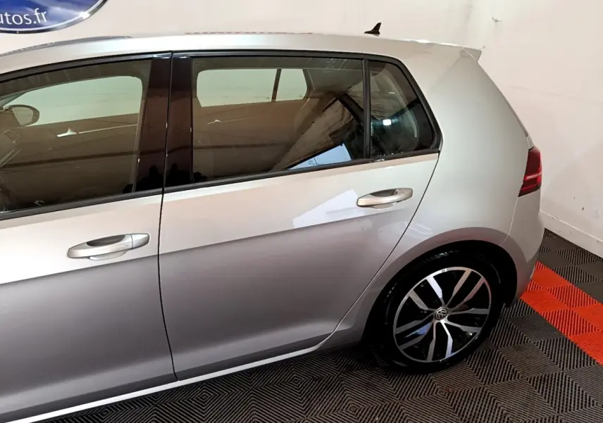 Vue latérale côté gauche d'une Volkswagen Golf gris clair avec jantes alliage et poignées de porte chromées.