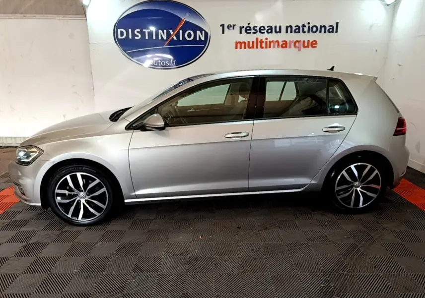 Profil côté gauche d'une Volkswagen Golf gris clair 2017, avec jantes alliage et poignées de porte chromées.