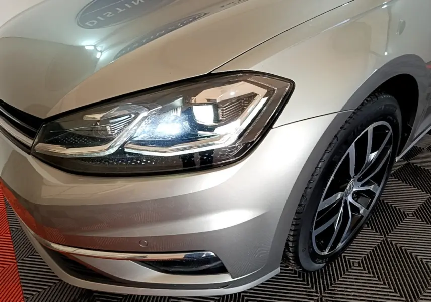 Gros plan sur l'avant droit d'une Volkswagen Golf gris clair, mettant en valeur le phare LED et la jante noire.