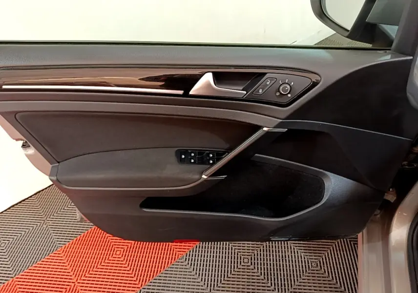 Vue du panneau de porte côté gauche de la Volkswagen Golf gris clair, avec commandes électriques et insert décoratif brillant.
