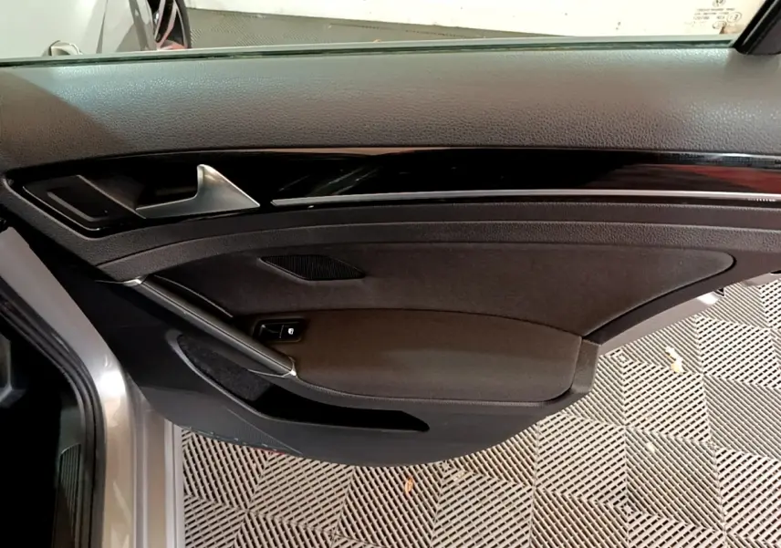 Porte côté gauche ouverte d'une Volkswagen Golf gris clair, montrant le panneau intérieur noir avec poignée argentée.