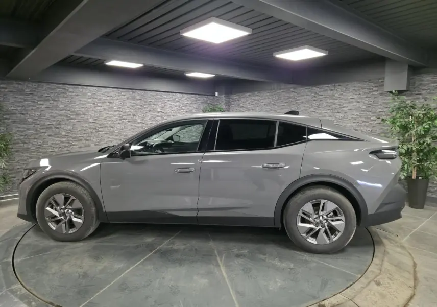 Peugeot 408 gris vue de profil côté gauche dans un showroom avec jantes alliage et vitres teintées.