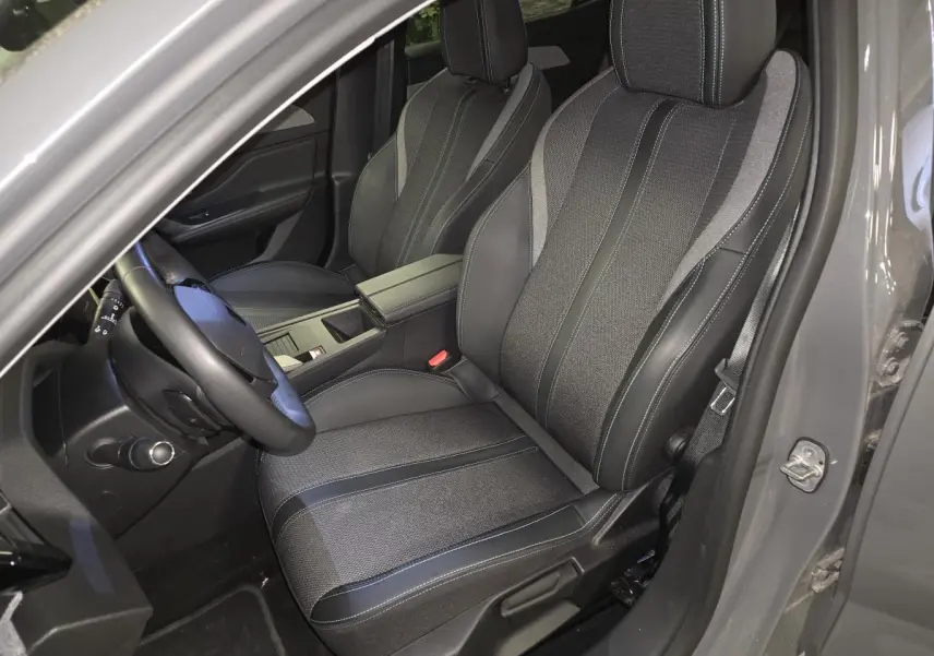 Vue intérieure côté conducteur de la Peugeot 408 gris, sièges tissu et cuir avec surpiqûres bleues et accoudoir central.