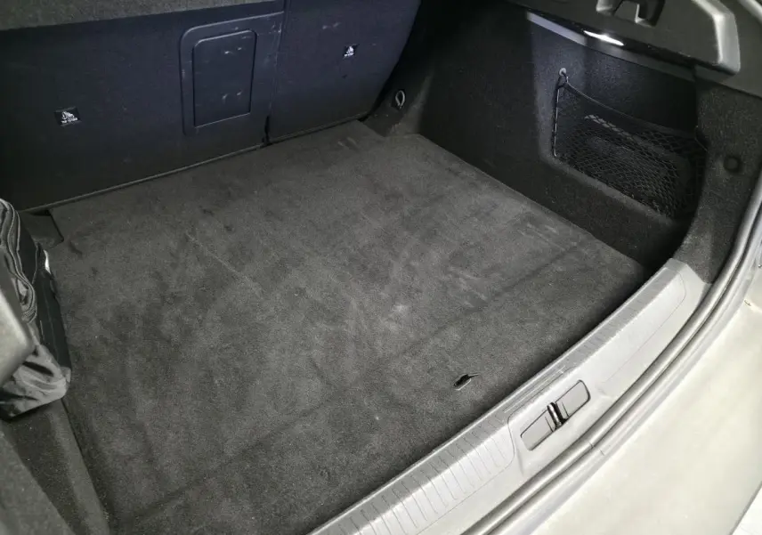 Vue rapprochée de la partie arrière du coffre gris du Peugeot 408 1.2i Hybrid avec tapis noir et filet de rangement latéral.