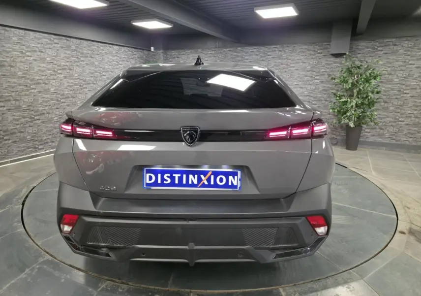 Vue arrière d'une Peugeot 408 gris métallisé avec feux LED allumés et logo lion central sur fond noir brillant.