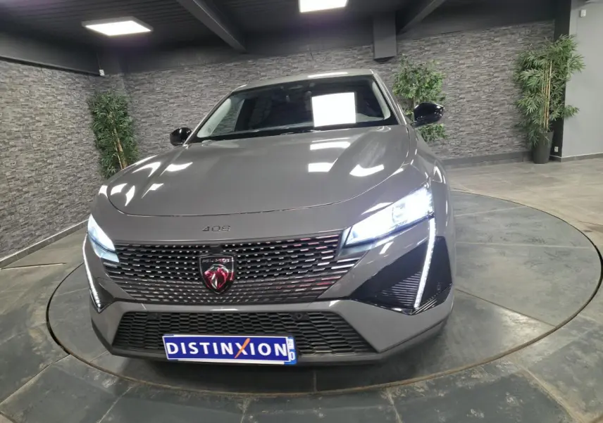 Vue avant d'une Peugeot 408 gris métallisé avec calandre noire et feux LED allumés dans un showroom.