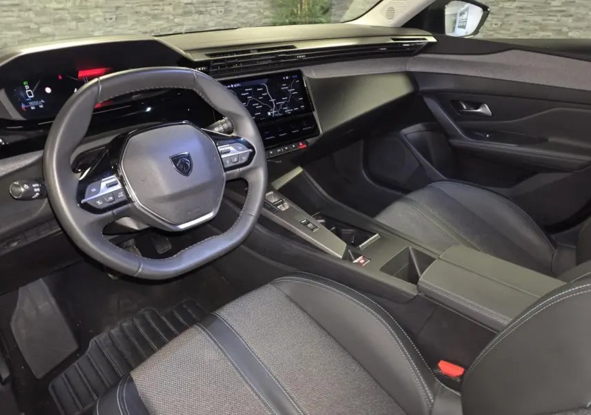 Vue intérieure côté conducteur du Peugeot 408 2025, avec tableau de bord numérique et sellerie tissu gris foncé.