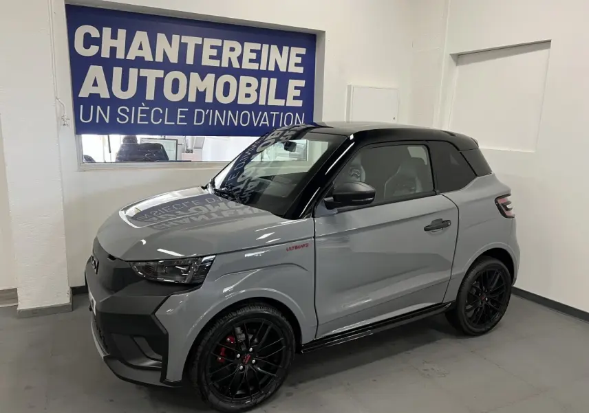 Vue 3/4 avant droite d'une Ligier JS50 grise avec toit noir et jantes noires en showroom.