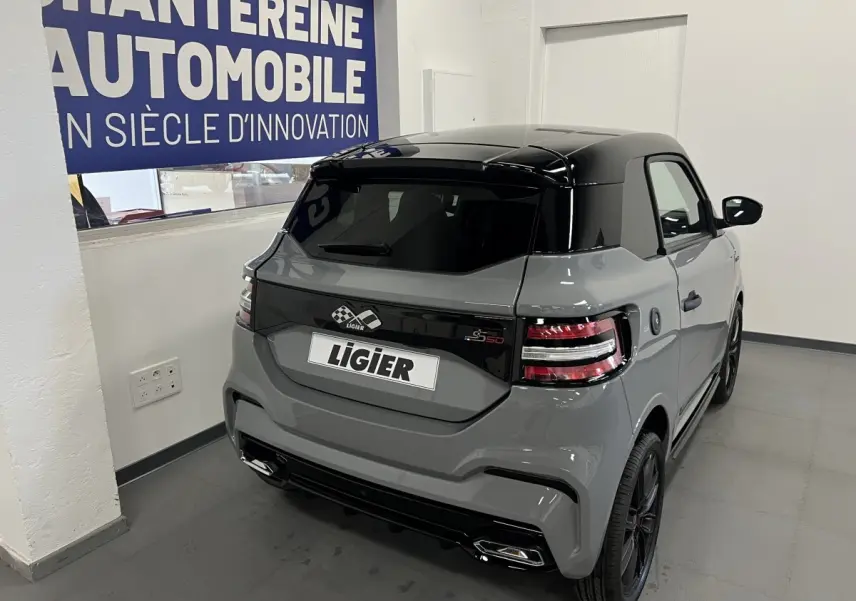 Vue 3/4 arrière droite d'une Ligier JS50 grise avec toit noir brillant et feux arrière LED en intérieur showroom.
