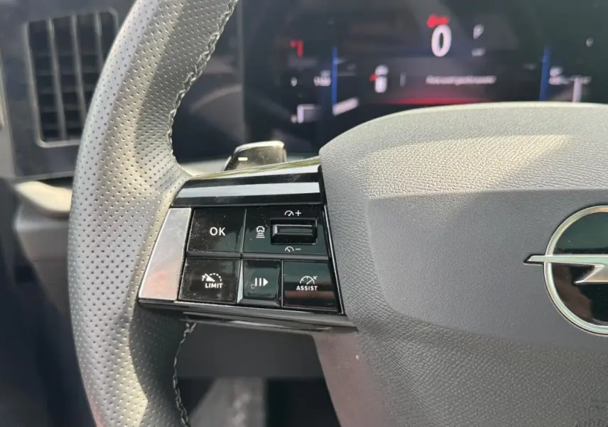 Gros plan sur le volant gris perforé de l’Opel Astra 2024 avec commandes multifonctions à gauche et logo central.