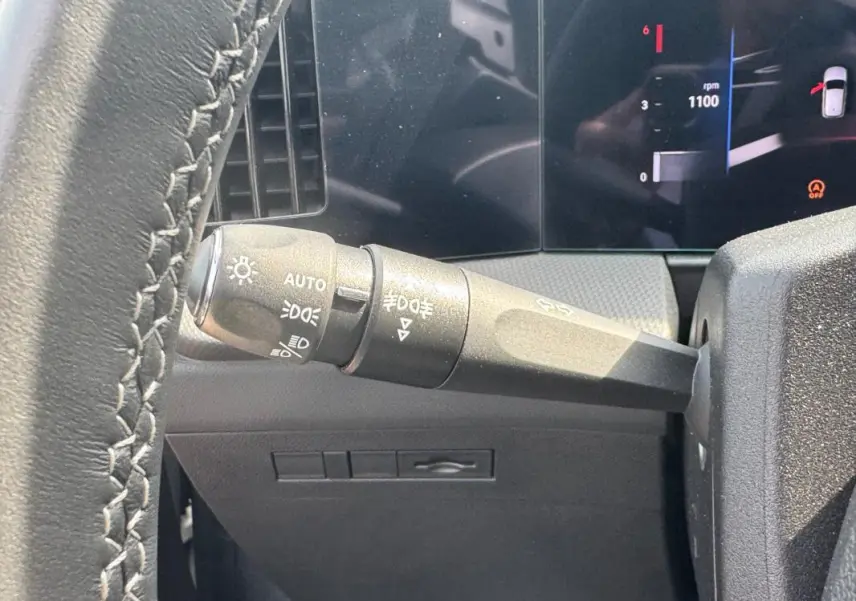 Gros plan sur le commodo d’éclairage à gauche du volant cuir de l’Opel Astra gris 2024, tableau de bord numérique visible.