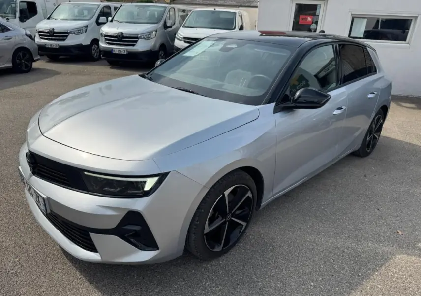 Opel Astra gris 3/4 avant droit avec toit noir, jantes alliage 17 pouces et vitres surteintées.