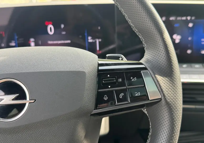Gros plan sur le volant cuir perforé gris de l’Opel Astra 2024 avec commandes intégrées et tableau de bord numérique flou.