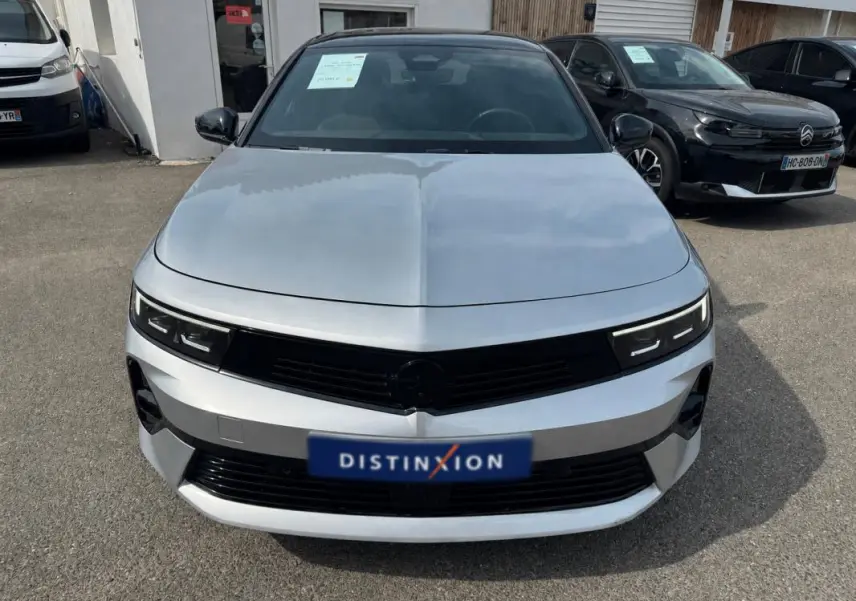 Vue avant d'une Opel Astra gris clair 2024 avec calandre noire et phares LED fins, stationnée en extérieur.