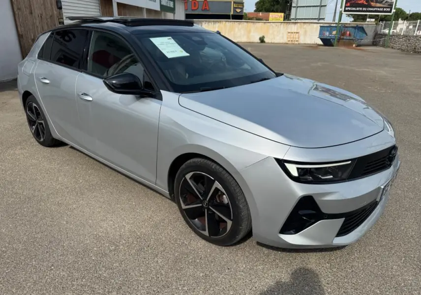 Vue 3/4 avant droite d'une Opel Astra gris clair avec jantes alliage noires et vitres surteintées.