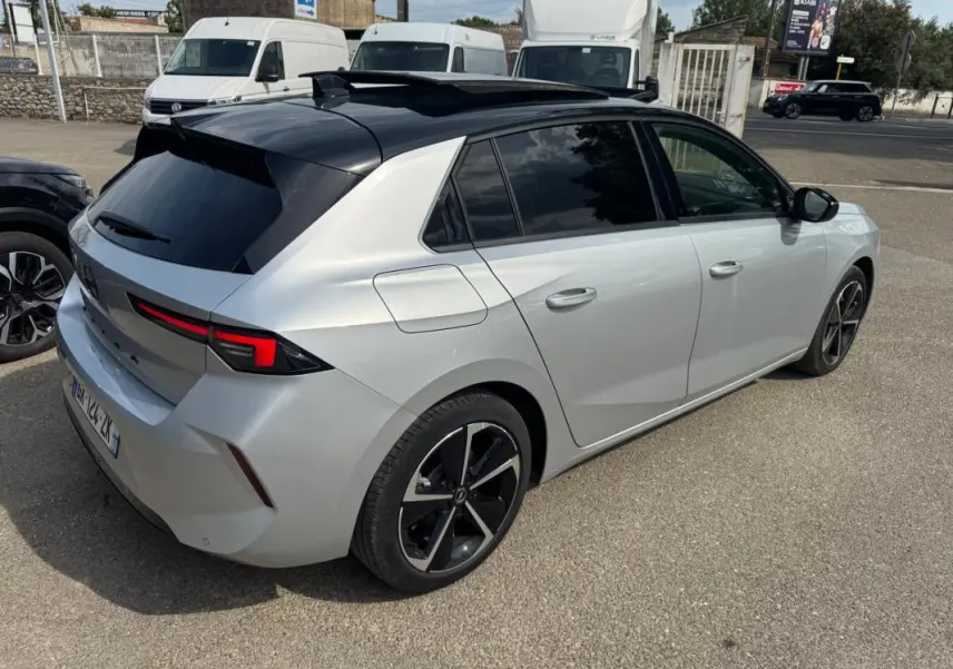 Opel Astra gris clair vue 3/4 arrière droit avec toit noir, jantes alliage 17 pouces et vitres surteintées.