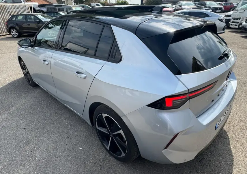 Opel Astra gris 3/4 arrière droit avec toit noir, vitres surteintées et jantes alliage 17 pouces.