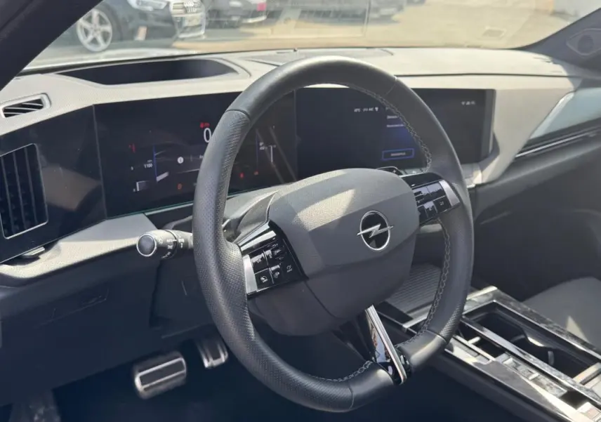 Vue intérieure centrée sur le volant cuir noir de l'Opel Astra 2024, avec tableau de bord numérique et console moderne.