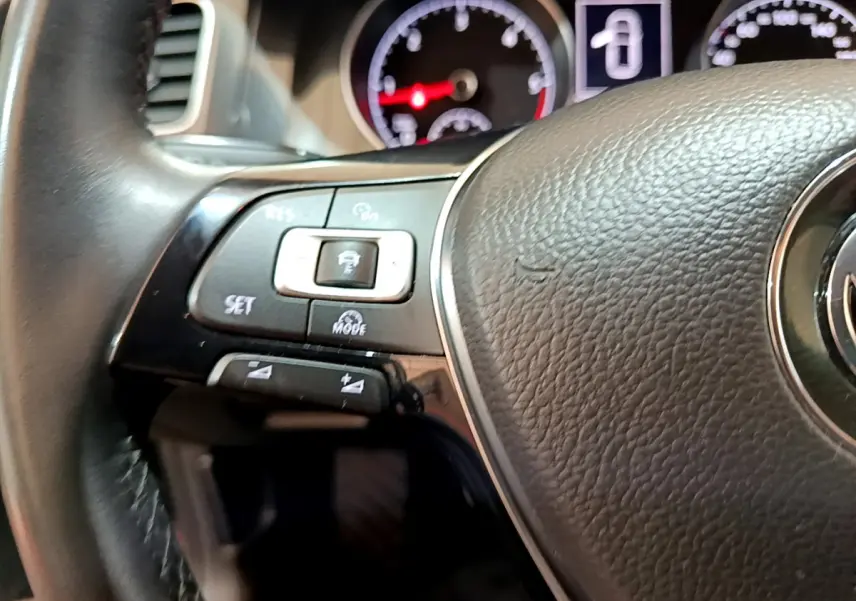 Gros plan sur le volant cuir noir de la Volkswagen Golf 2018, avec commandes multifonctions et tableau de bord éclairé.