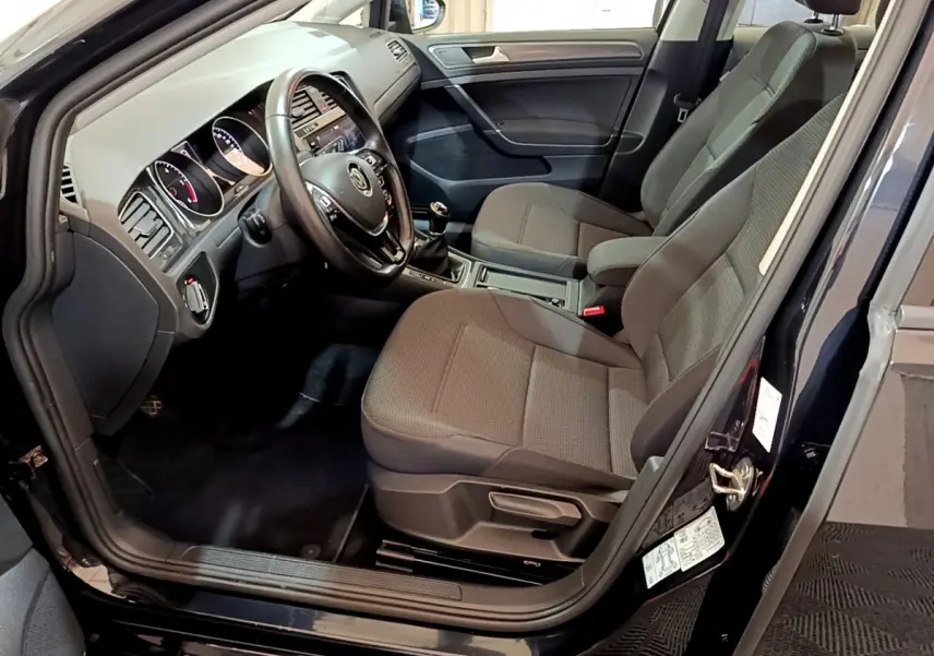 Intérieur avant droit d'une Volkswagen Golf noire 2018, sièges tissu gris et tableau de bord avec volant cuir.