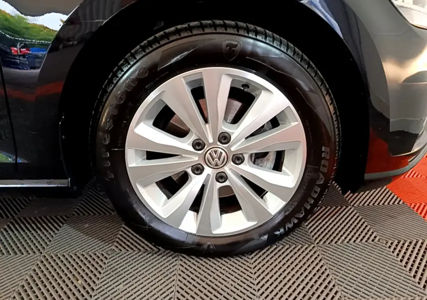 Gros plan sur la roue avant gauche d'une Volkswagen Golf noire, jante alliage argentée avec logo VW au centre.