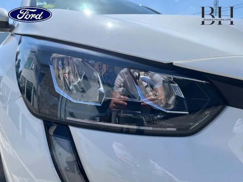 Gros plan sur le phare avant droit de la Peugeot 208 blanc banquise, mettant en valeur son design moderne et anguleux.