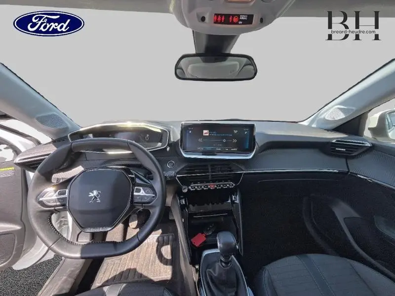 Vue intérieure avant de la Peugeot 208 blanche, volant compact et écran tactile central visible.