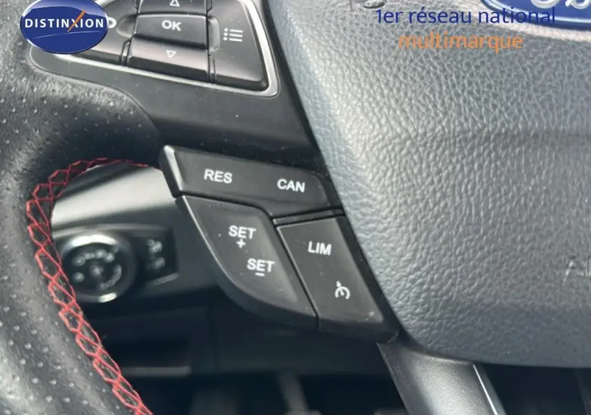Gros plan sur le volant en cuir noir avec surpiqûres rouges du Ford EcoSport gris clair, boutons de régulateur de vitesse visibles.