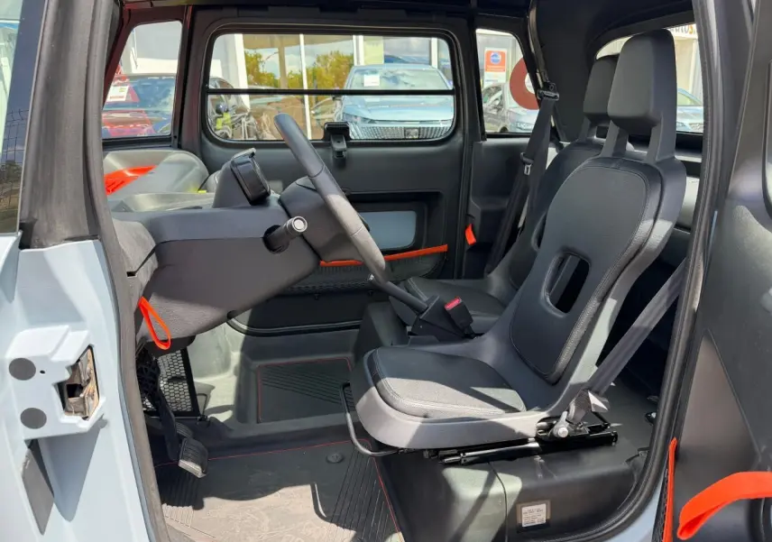 Intérieur côté conducteur du Citroën Ami MY AMI POP 2024, sièges noirs et détails orange, volant et tableau de bord minimalistes.