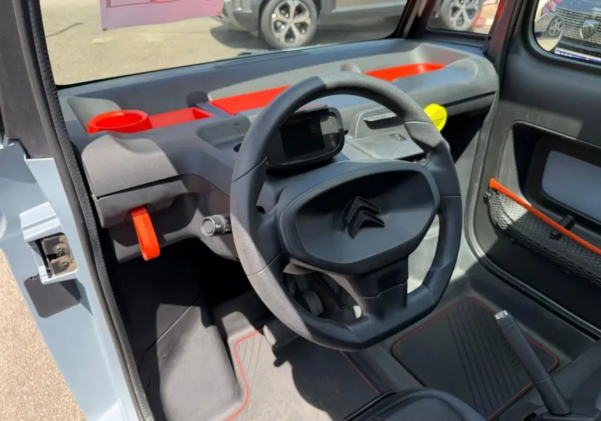 Vue intérieure côté conducteur du tableau de bord noir et gris avec touches orange vif de la Citroën Ami MY AMI POP 2024.