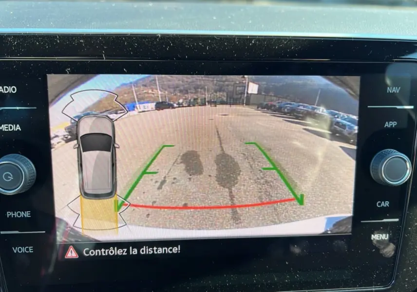 Vue de la caméra de recul du Volkswagen T-Cross blanc pur, affichant les lignes de guidage et l'alerte de distance.
