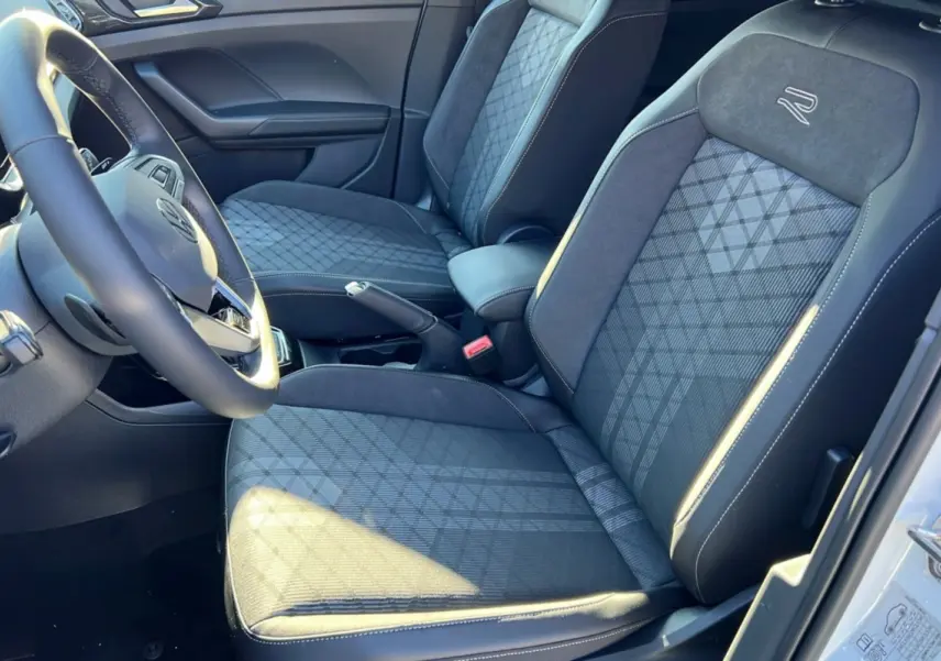 Vue intérieure côté conducteur du Volkswagen T-Cross blanc, sièges tissu R-Line avec surpiqûres et volant cuir multifonctions.