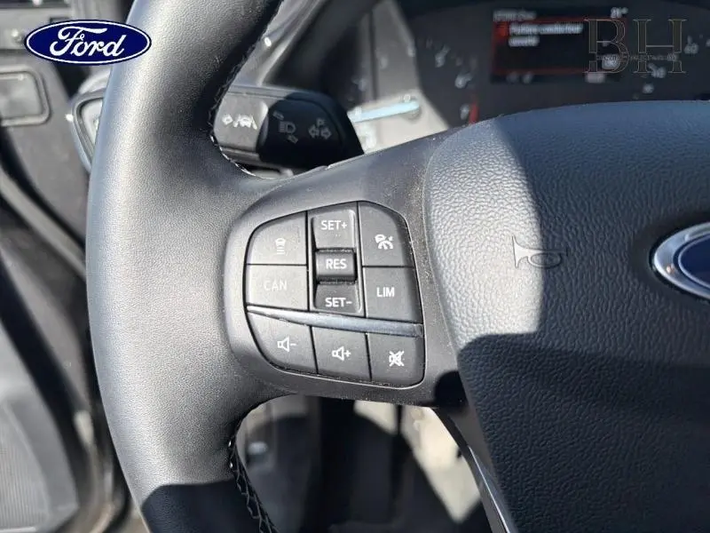 Gros plan sur les commandes au volant noir du Ford Puma 2024, mettant en valeur les boutons de régulateur et volume sonore.