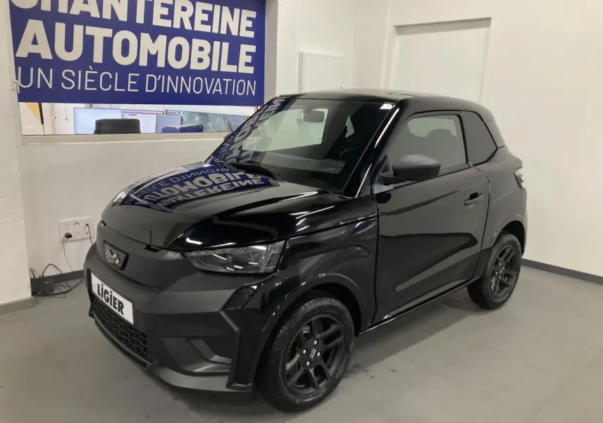 Vue 3/4 avant droite de la Ligier JS50 noire 2026 avec jantes alu noires et feux à LED en intérieur showroom.