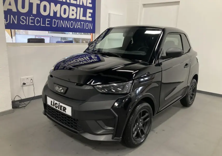 Vue 3/4 avant d'une Ligier JS50 noire 2026 avec jantes alu noires et feux LED en intérieur showroom.